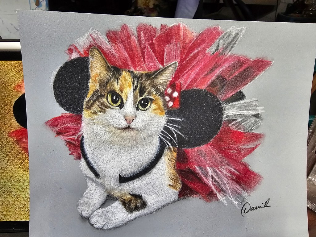 Calico cat portrait with a dramatic red, white, and black fan-like ruff on a gray background.
