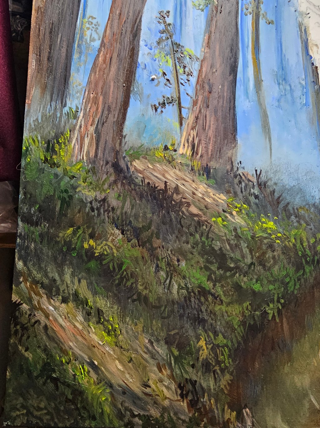 Close view of a forest landscape painting in progress, with tall tree trunks and blue light between the trees.